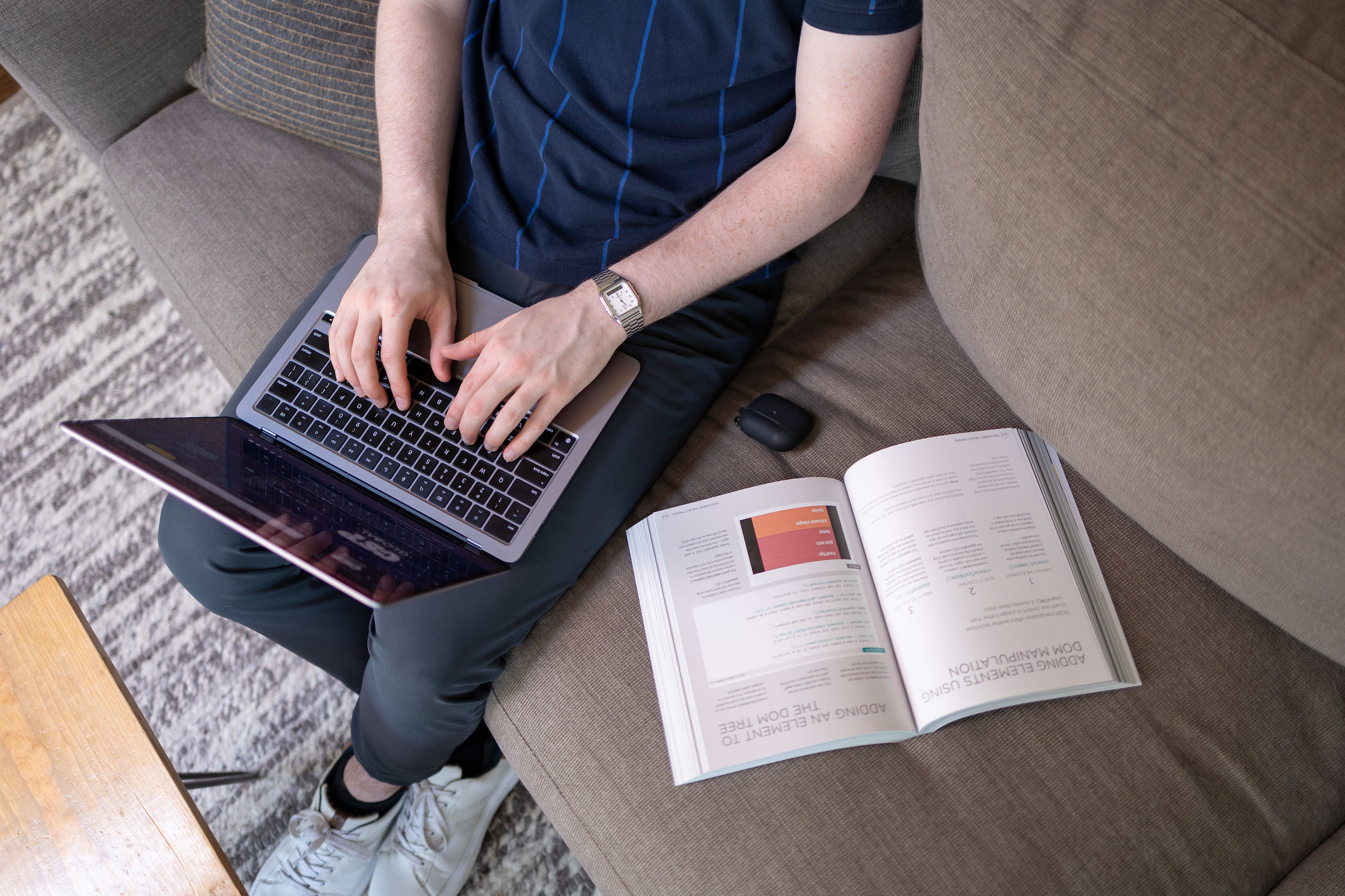 Student sitting on a couch using a laptop and an open book.