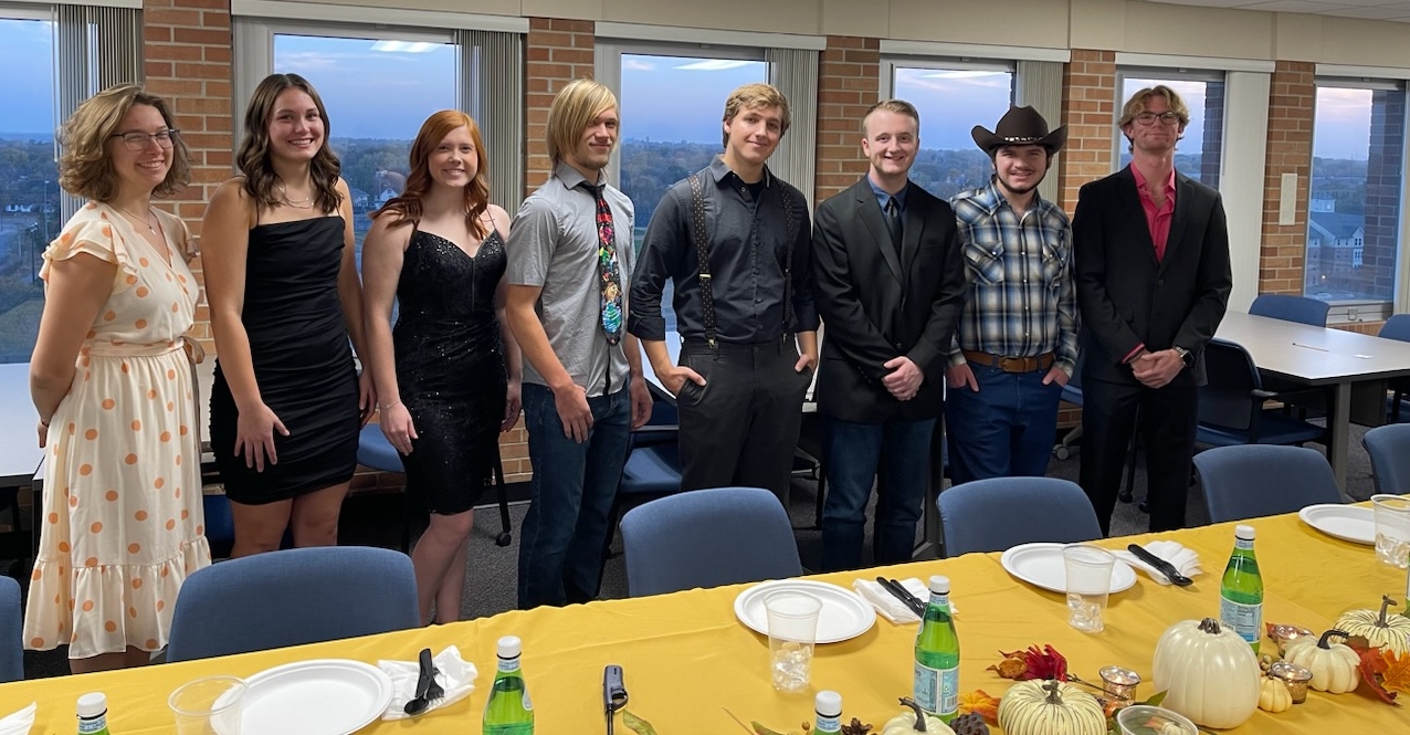 Group of students smiling for a photo behind a dinner table.