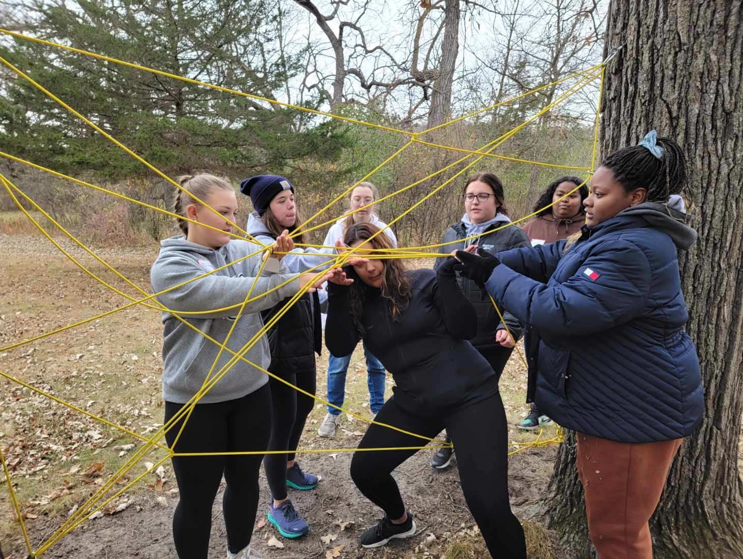 students participating in a team building exercise outside. Navigating student through a collection of thin ropes