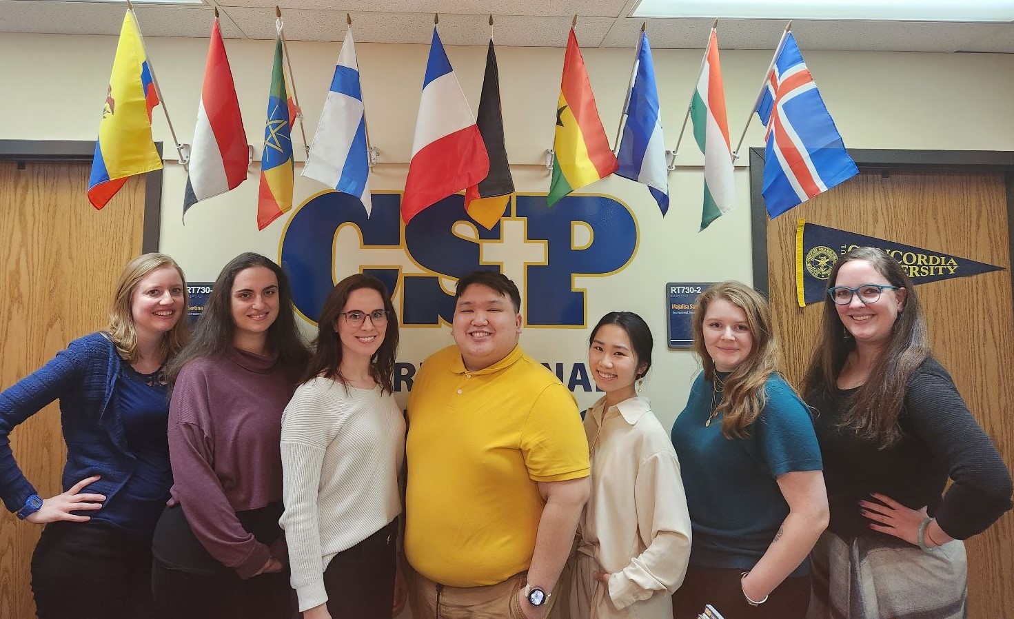 International Student Services staff standing in front of office. Flags above them