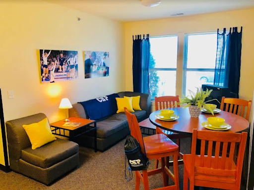 Dorm living room with high top table and four chairs with a grey couch and window