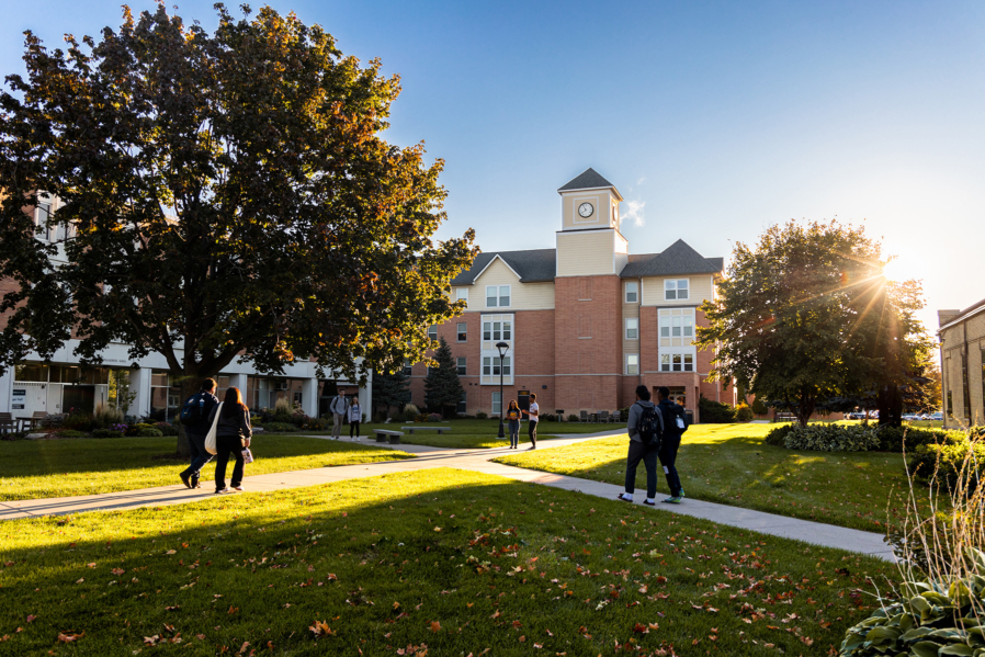 Groups of students walking across the campus green in front of Holst Hall in autumn.