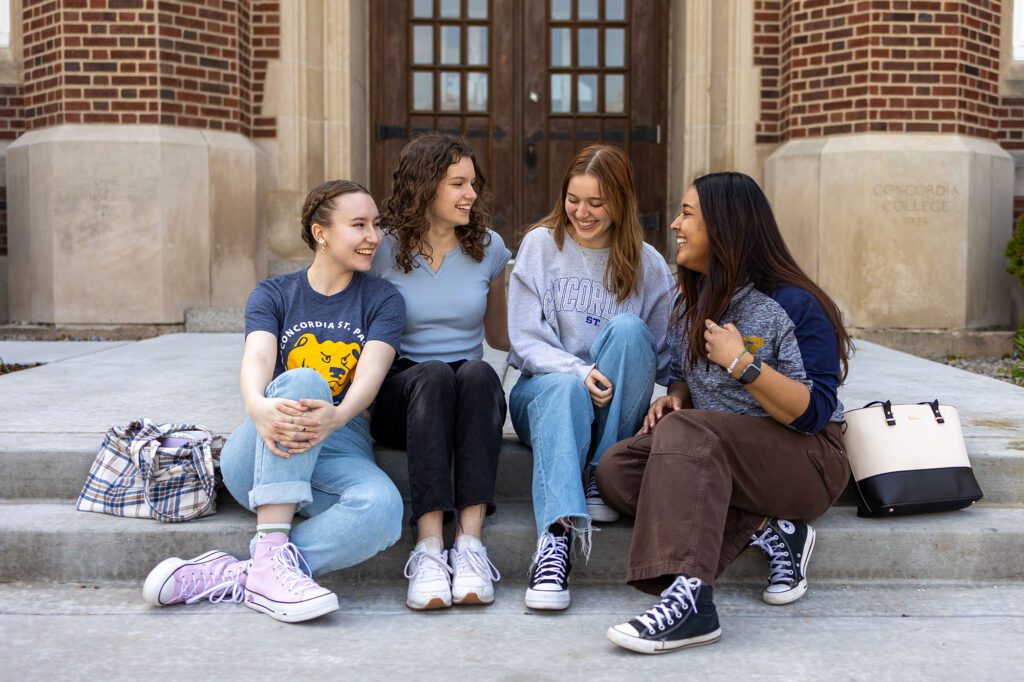 Four students sitting on a step in front of a CSP academic building.