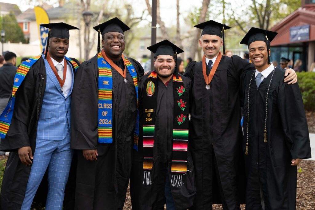 Group of five students standing together at commencement wearing their caps and gowns.