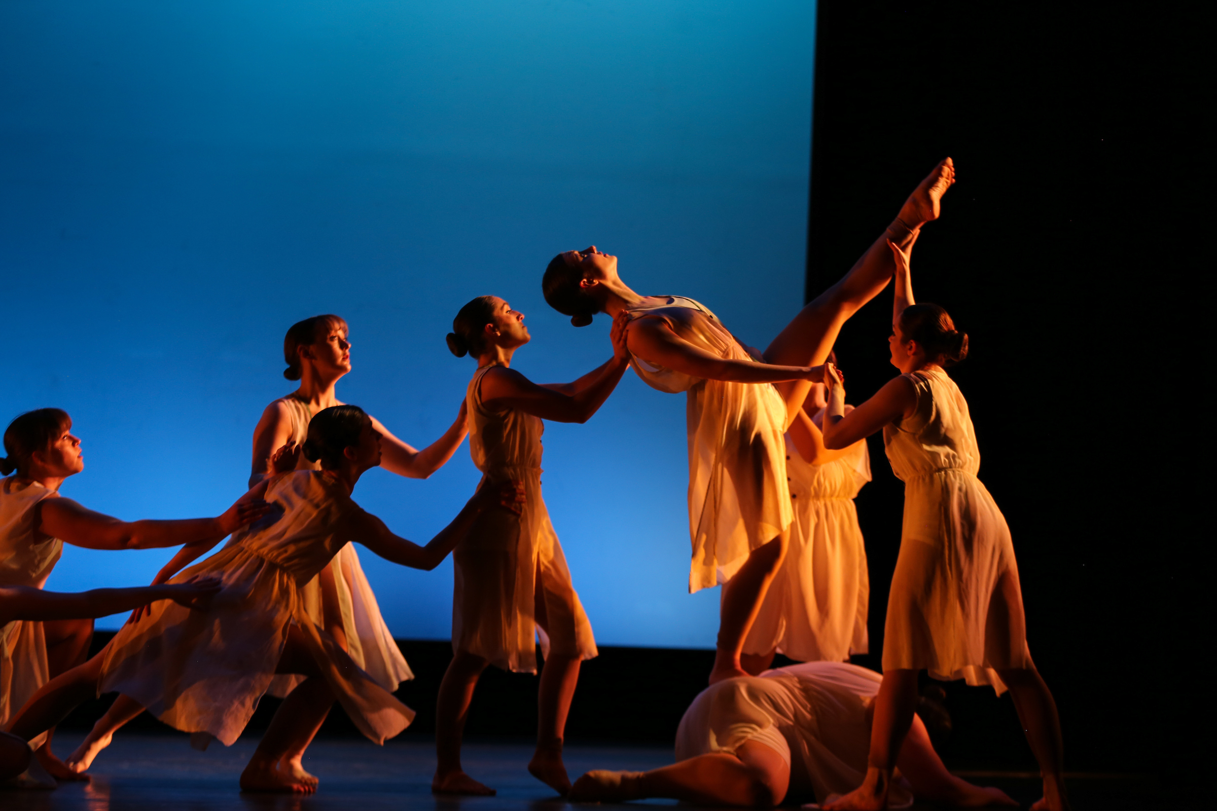 Students performing a dance routine on stage with a bright blue background.