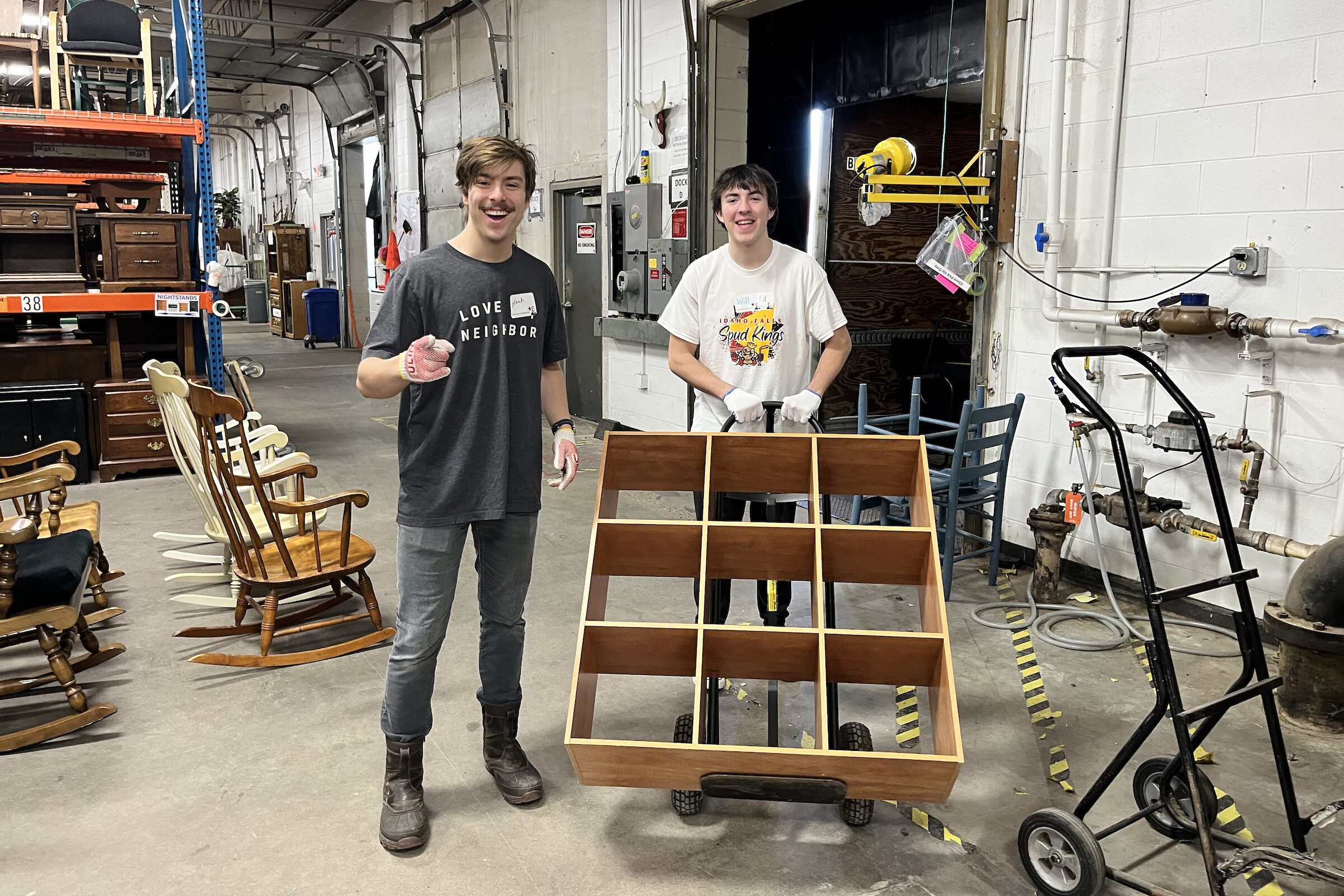 Two students helping move furniture in a warehouse for a service event.