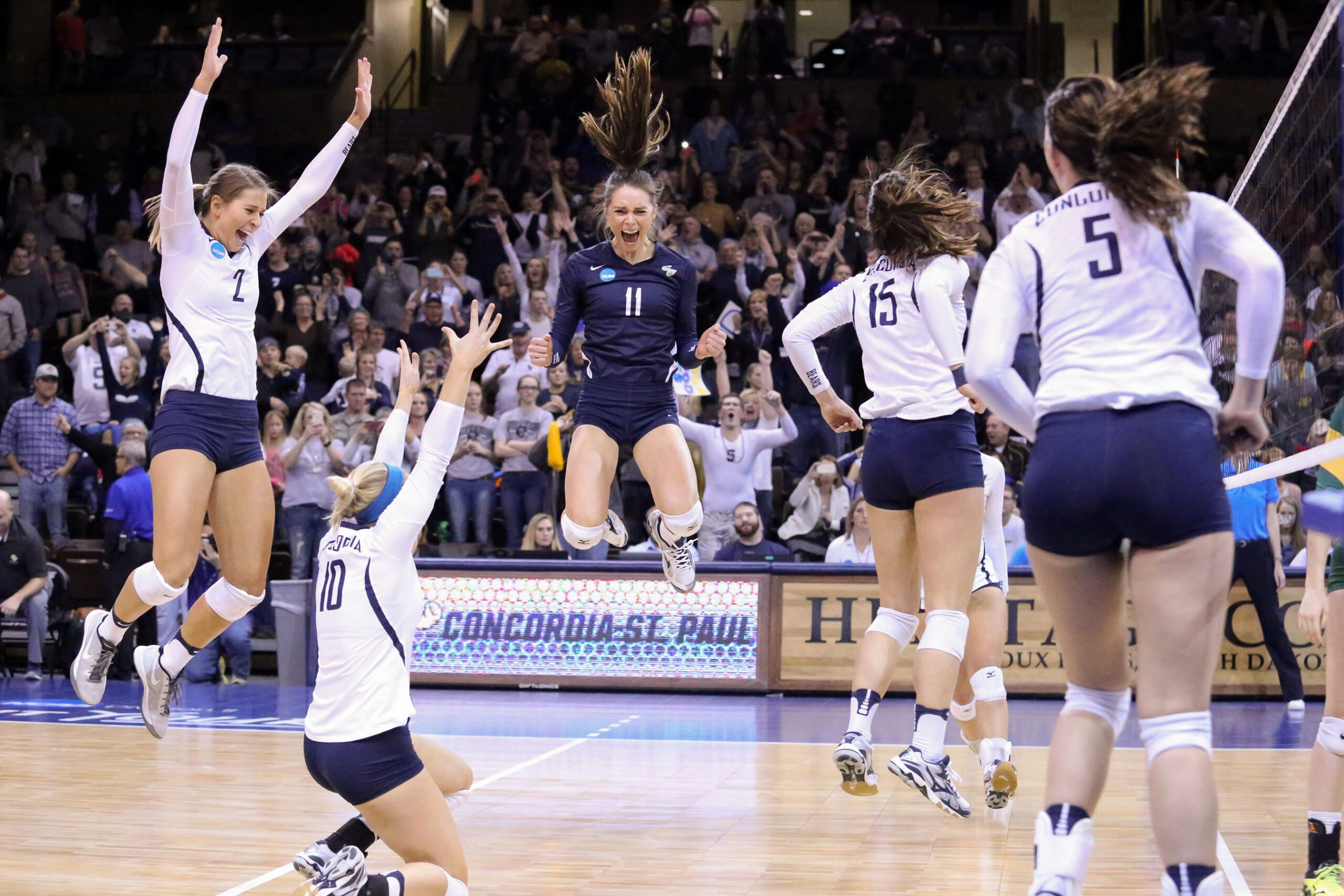 CSP volleyball players jumping and celebrating a win on the court.