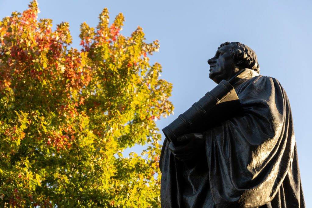 Bronze statue of Martin Luther outdoors in front of a green tree starting to turn orange for autumn.