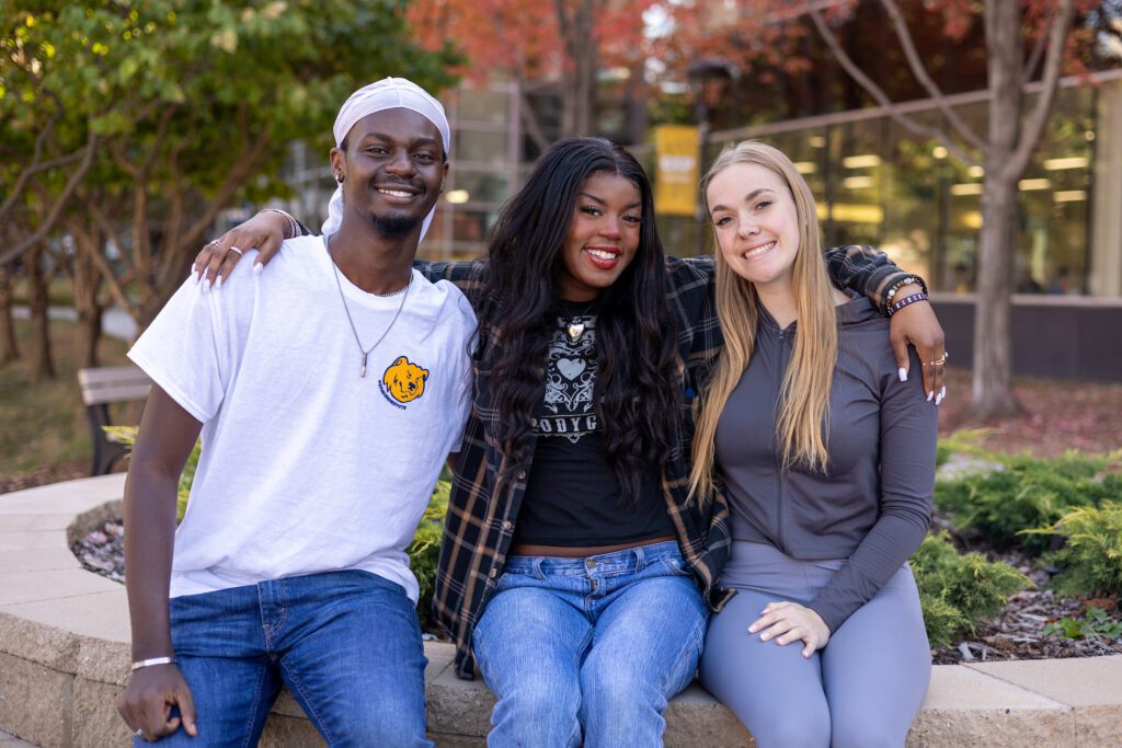 Group of three students sitting together outside and smiling.