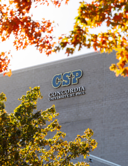 Gray building with a blue CSP logo sign on it behind two trees.