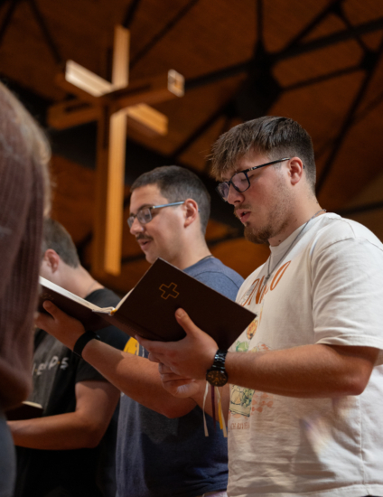 Two students holding hymnals singing in chapel.