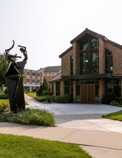 Brown chapel building with statue in front.