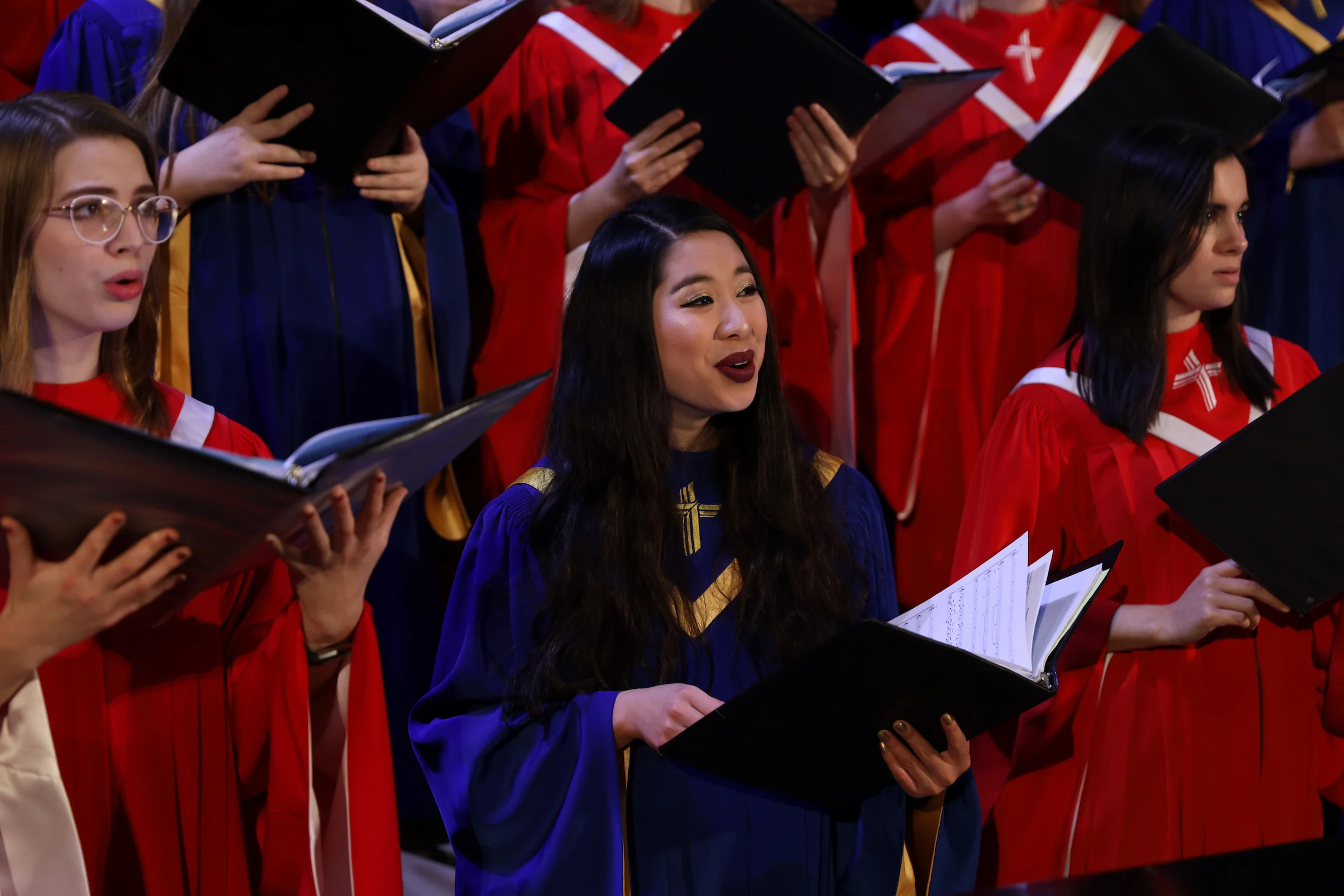 Group of choir students performing together at CSP wearing blue and red robes and holding song books.