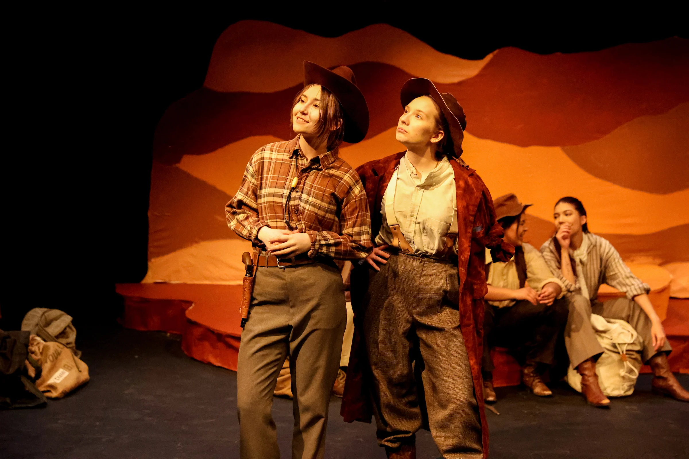 Four students on stage wearing old western clothing in a play performance.