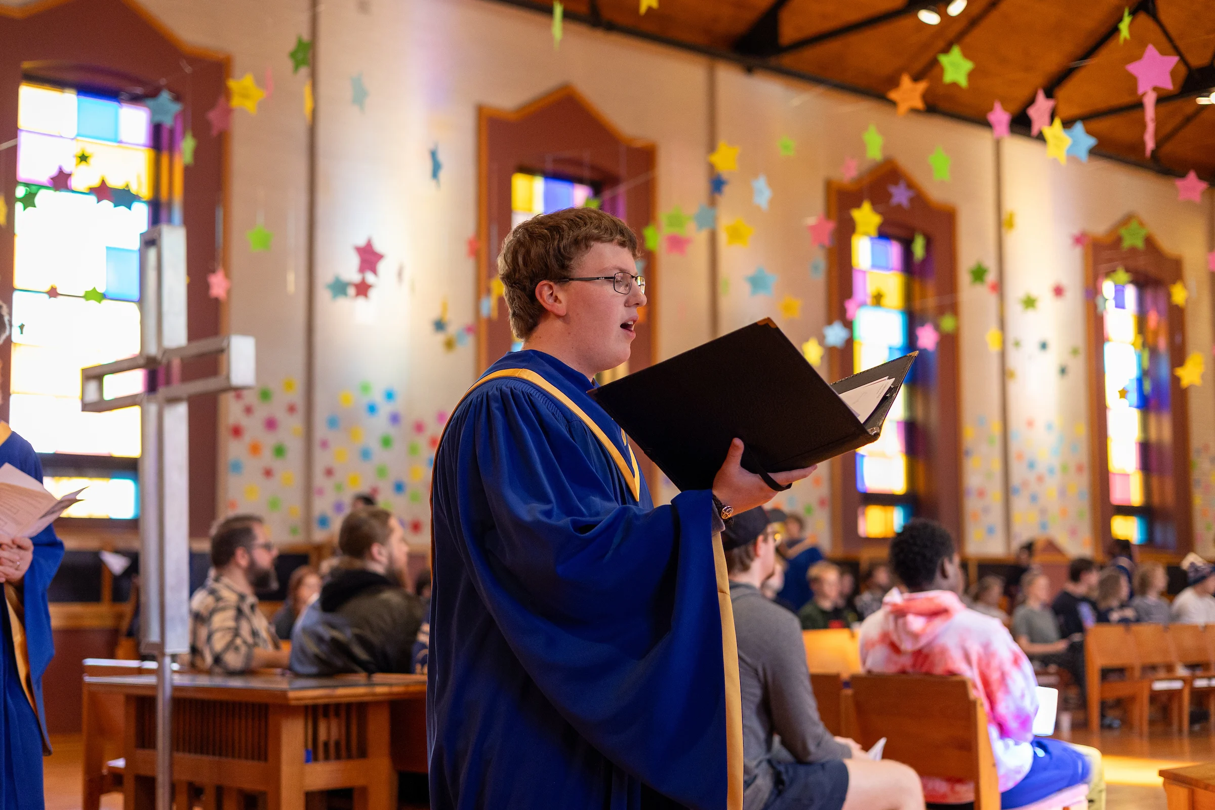 Student wearing blue choir robes and holding a song book singing inside CSP's chapel.