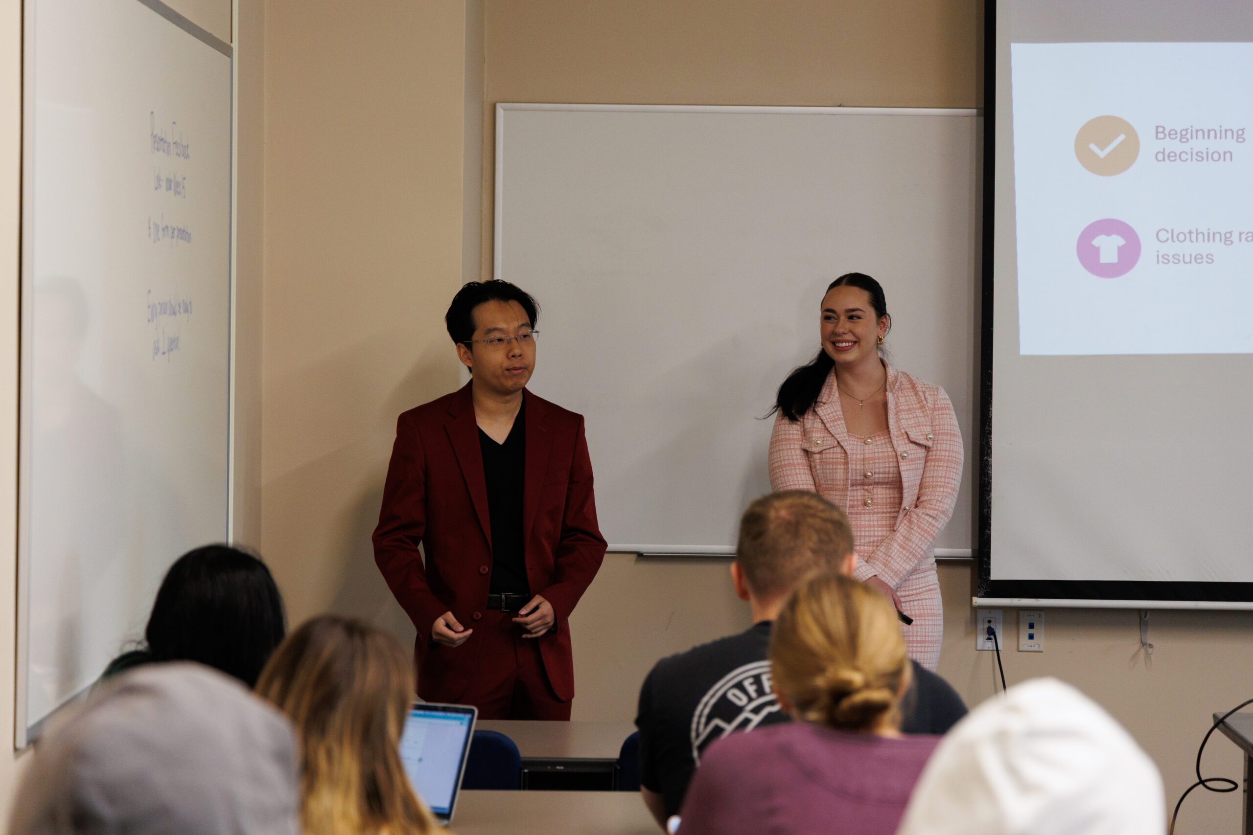 Two students standing in front of a white board giving a presentation.