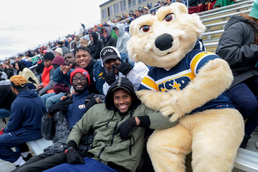 Large group of CSP students sitting in bleachers with CSP's mascot, Comet.