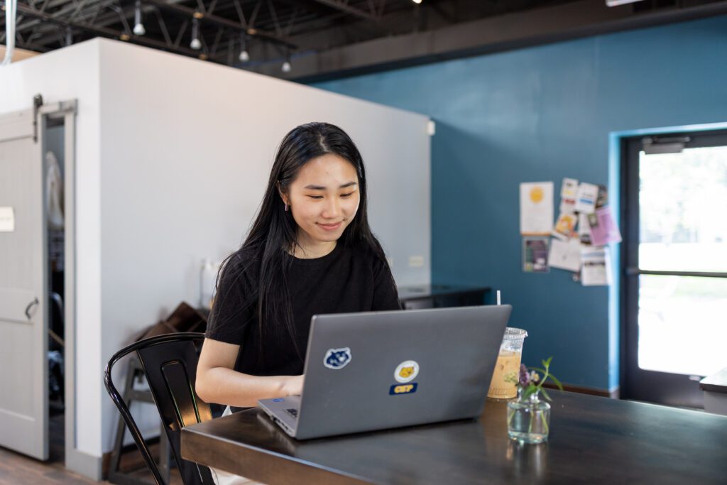 CSP student sitting at a table in a coffee shop using a laptop.
