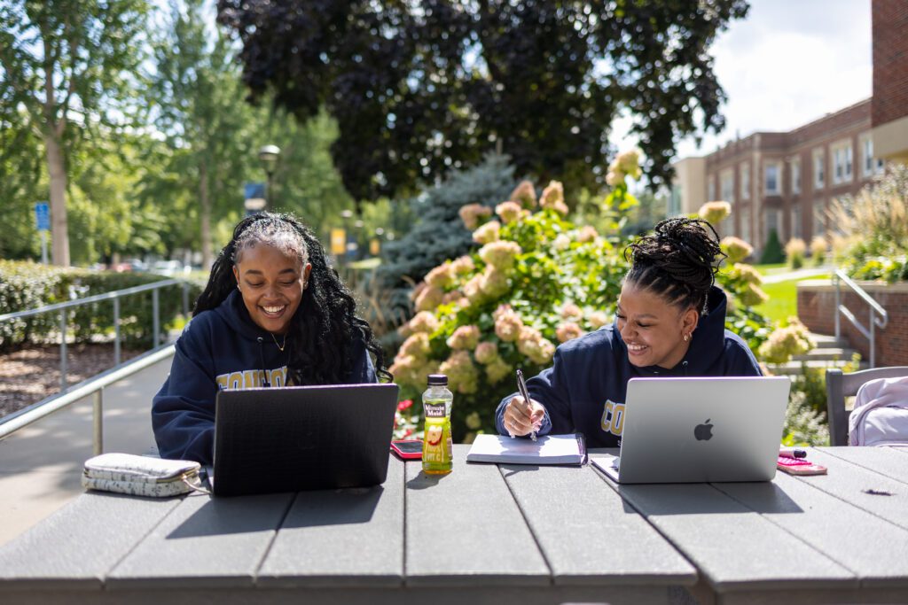 Two CSP students sitting at an outdoor table using laptops.