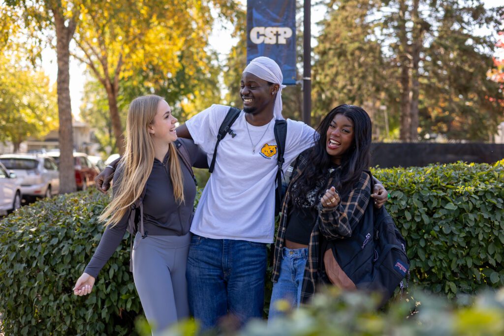 Group of three CSP students standing together outside in front of a blue CSP banner.