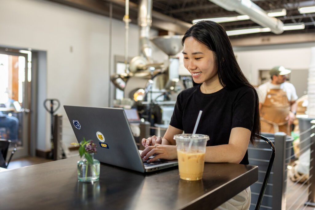 CSP Global student sitting at a table in a coffee shop using a laptop.